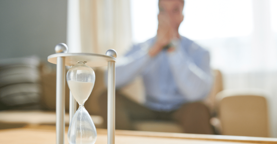 Waiting for commercial construction costs to decrease, stressed out business man watches time pass through hourglass.